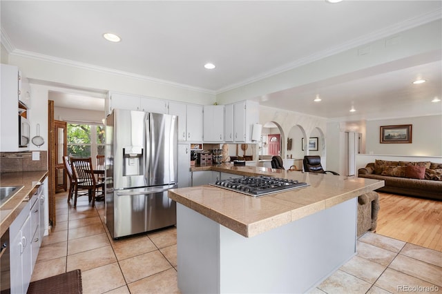kitchen with light tile patterned flooring, appliances with stainless steel finishes, arched walkways, open floor plan, and ornamental molding