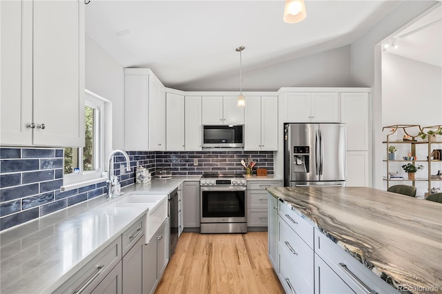 7767 S Depew St, Littleton, CO 80128 - kitchen with stainless steel appliances, vaulted ceiling, light stone countertops, decorative backsplash, and light wood finished floors