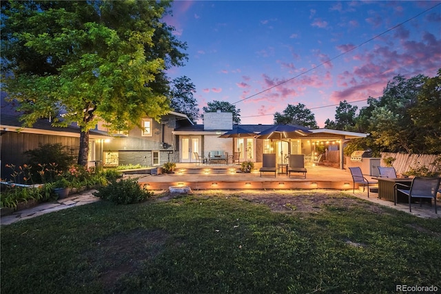 7767 S Depew St, Littleton, CO 80128 - back of property at dusk with french doors, a wooden deck, a fire pit, and stone siding
