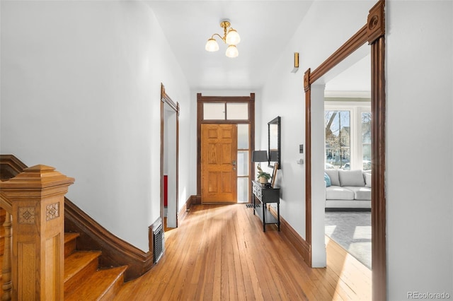 entrance foyer featuring stairway, visible vents, baseboards, light wood-type flooring, and a chandelier