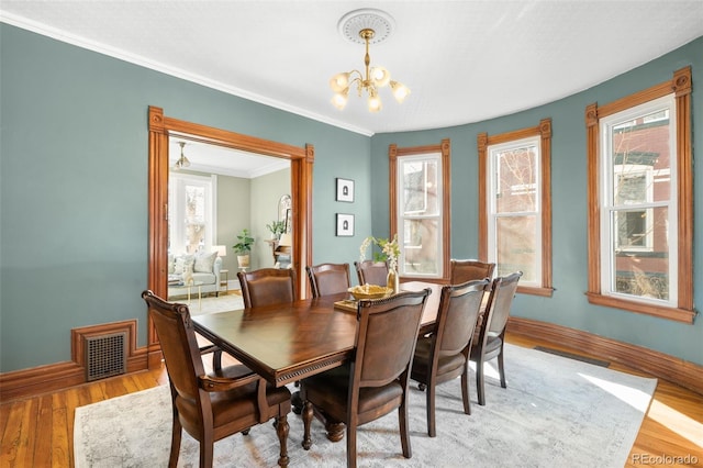 dining space featuring baseboards, visible vents, crown molding, light wood-type flooring, and a chandelier