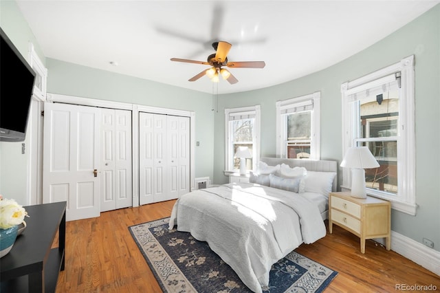 bedroom featuring visible vents, baseboards, light wood-style flooring, ceiling fan, and two closets