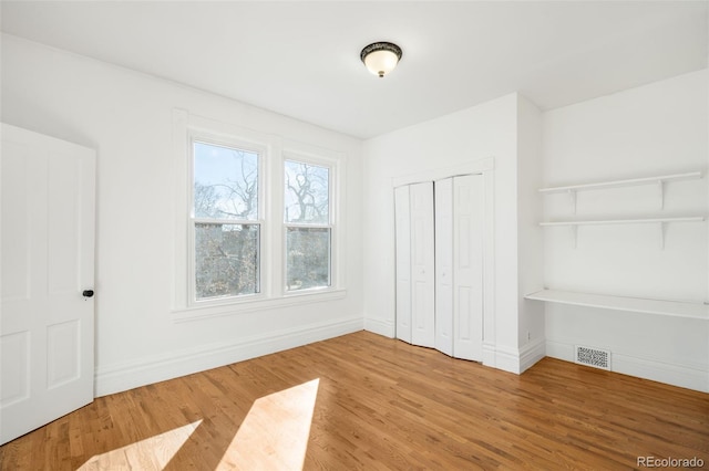 unfurnished bedroom featuring visible vents, baseboards, a closet, and wood finished floors