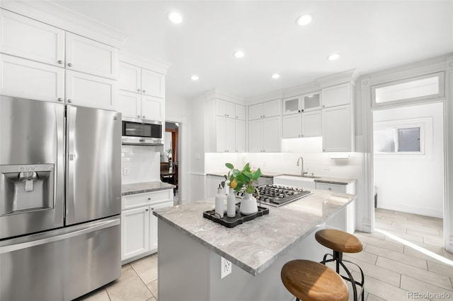 kitchen featuring a kitchen island, appliances with stainless steel finishes, a kitchen breakfast bar, white cabinets, and a sink