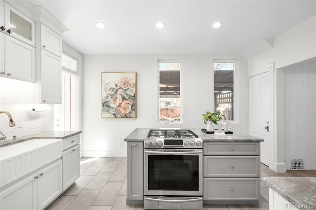 kitchen with visible vents, light stone counters, recessed lighting, stainless steel range with gas cooktop, and glass insert cabinets