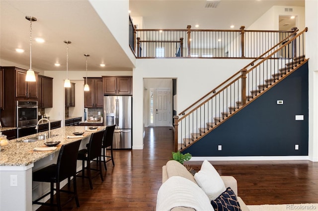 kitchen with appliances with stainless steel finishes, dark hardwood / wood-style floors, light stone countertops, hanging light fixtures, and sink