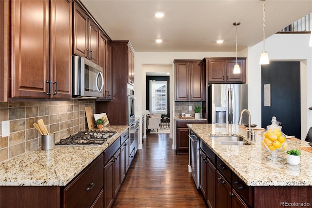 kitchen featuring a center island with sink, sink, appliances with stainless steel finishes, dark hardwood / wood-style floors, and hanging light fixtures