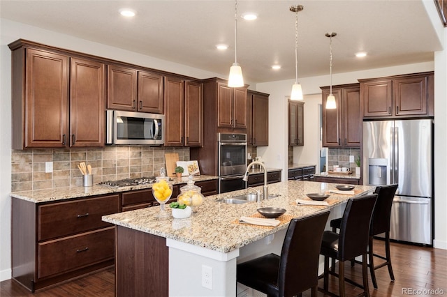 kitchen featuring a center island with sink, stainless steel appliances, decorative light fixtures, dark hardwood / wood-style flooring, and sink