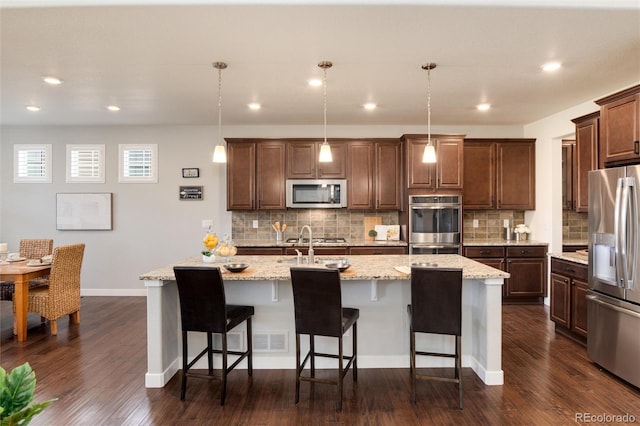 kitchen featuring dark hardwood / wood-style flooring, appliances with stainless steel finishes, decorative light fixtures, and a kitchen island with sink