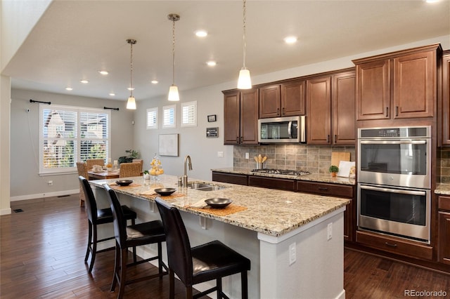 kitchen with stainless steel appliances, a center island with sink, sink, dark hardwood / wood-style floors, and pendant lighting