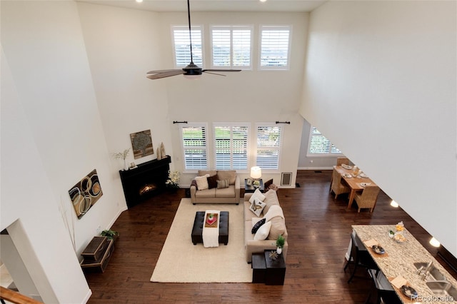 living room with dark wood-type flooring, ceiling fan, and a high ceiling