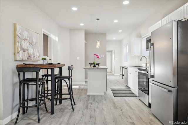 kitchen featuring sink, light hardwood / wood-style flooring, appliances with stainless steel finishes, decorative light fixtures, and white cabinetry