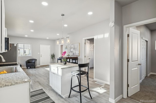 kitchen with white cabinetry, sink, a kitchen island, and hanging light fixtures