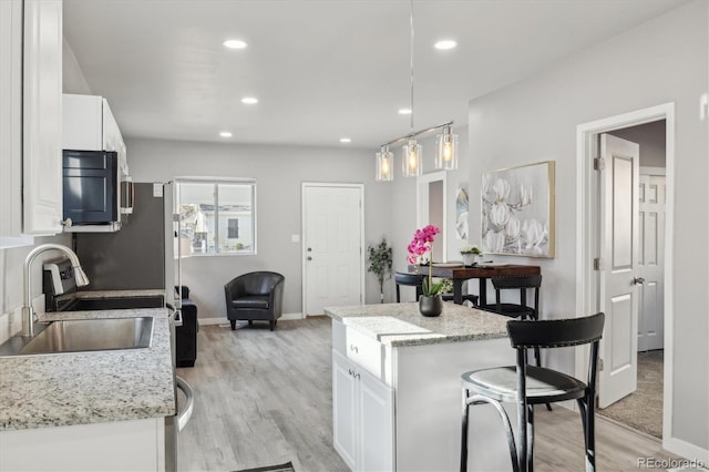 kitchen with sink, white cabinets, hanging light fixtures, and light hardwood / wood-style floors