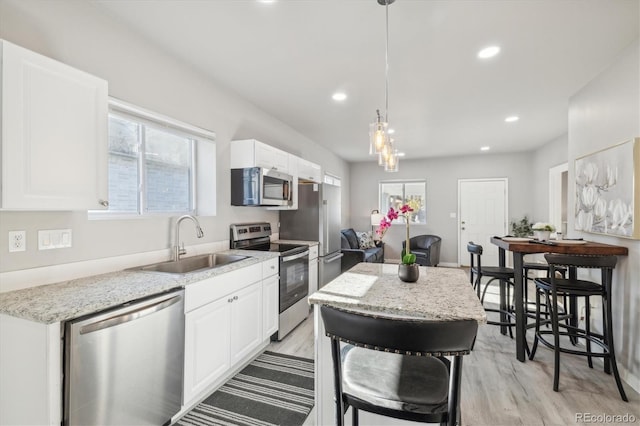 kitchen with white cabinets, hanging light fixtures, sink, light hardwood / wood-style flooring, and appliances with stainless steel finishes