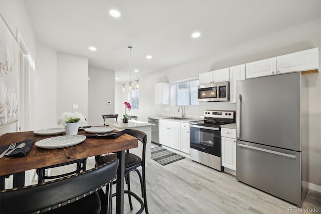 kitchen with sink, appliances with stainless steel finishes, decorative light fixtures, light hardwood / wood-style floors, and white cabinetry