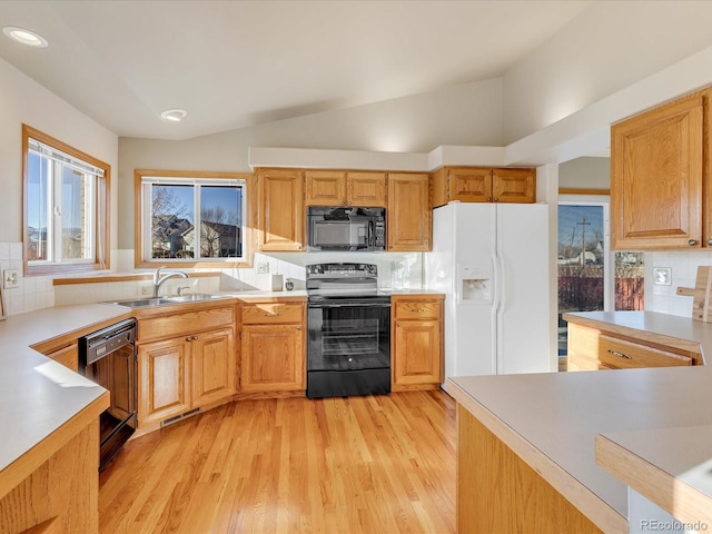 kitchen with backsplash, lofted ceiling, black appliances, light hardwood / wood-style flooring, and sink