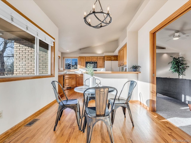 dining space with ceiling fan with notable chandelier, vaulted ceiling, and light wood-type flooring