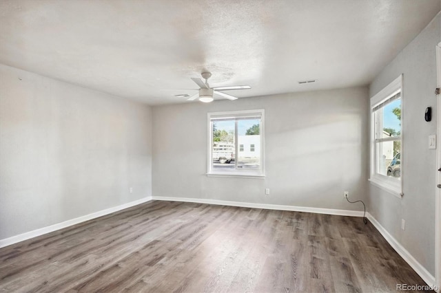 spare room with a wealth of natural light, visible vents, wood finished floors, and ceiling fan
