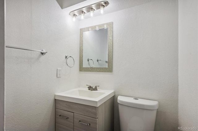 bathroom with toilet, vanity, and a textured wall