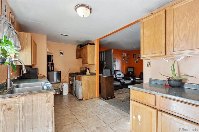 kitchen with a sink, visible vents, light tile patterned floors, stainless steel gas range, and light brown cabinets