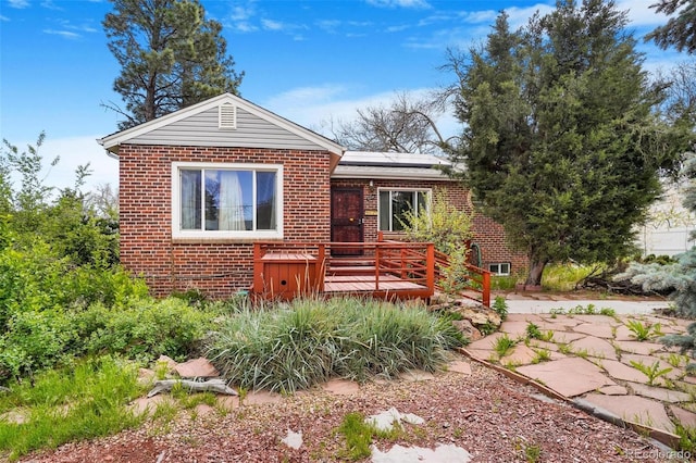 view of front of house with brick siding, solar panels, and a wooden deck