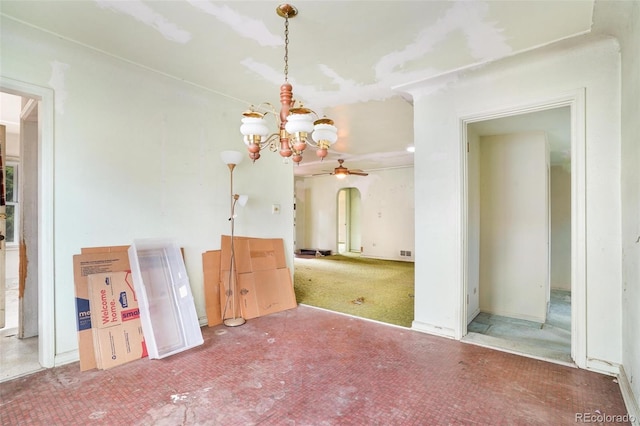 unfurnished dining area featuring carpet flooring, arched walkways, and ceiling fan with notable chandelier