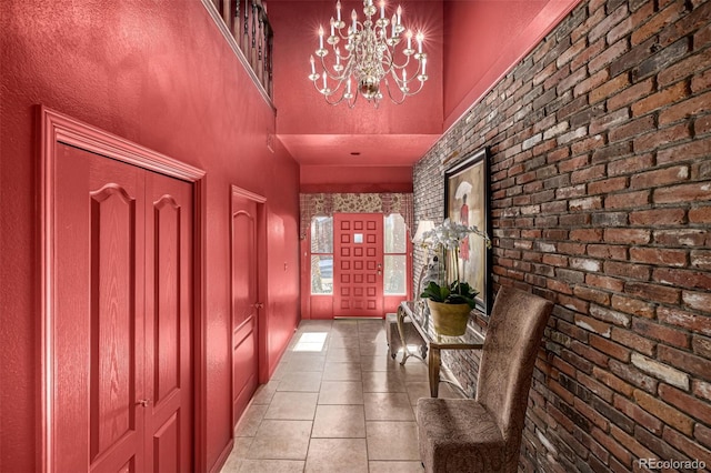 entrance foyer featuring light tile patterned floors, a notable chandelier, brick wall, and a high ceiling