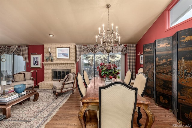 dining area with an inviting chandelier, a brick fireplace, a wealth of natural light, and hardwood / wood-style floors