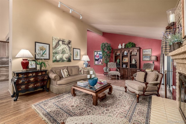 living room featuring vaulted ceiling, light wood-type flooring, track lighting, and a fireplace