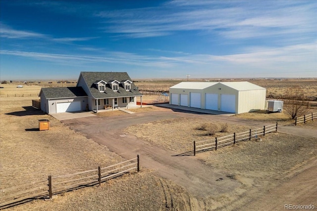 view of front of house with an outbuilding, driveway, a detached garage, fence, and a rural view