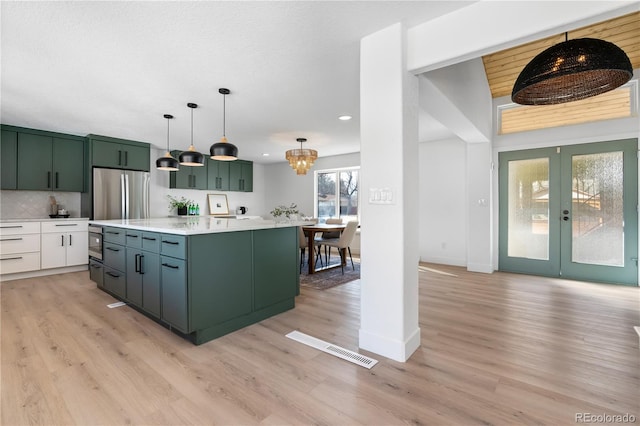 kitchen with a kitchen island, stainless steel refrigerator, decorative light fixtures, tasteful backsplash, and light hardwood / wood-style flooring