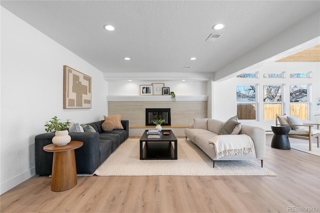 living room with a tile fireplace, a textured ceiling, and light wood-type flooring