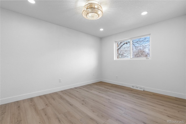 unfurnished room with a textured ceiling and light wood-type flooring