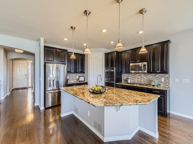 kitchen featuring dark wood-type flooring, stainless steel appliances, tasteful backsplash, and a center island with sink