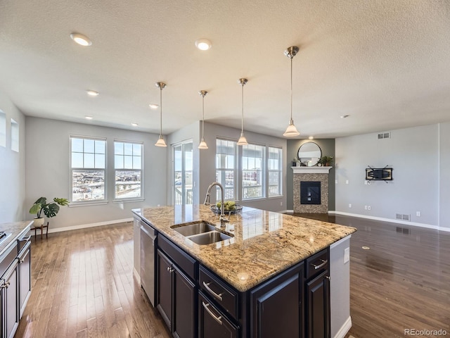 kitchen featuring sink, stainless steel dishwasher, dark hardwood / wood-style floors, pendant lighting, and a kitchen island with sink