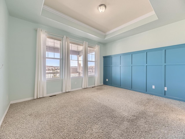 carpeted empty room featuring a raised ceiling and crown molding