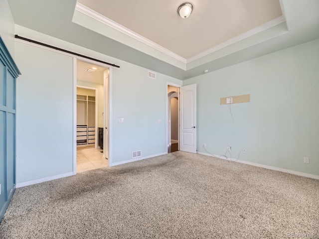 unfurnished bedroom with a raised ceiling, a walk in closet, light carpet, and a closet