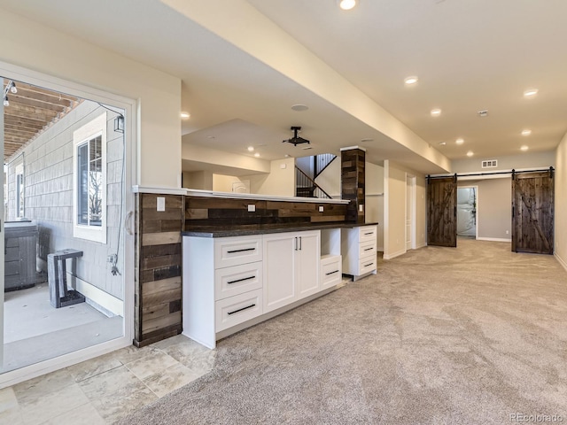 kitchen featuring white cabinetry, ceiling fan, a barn door, dark stone counters, and light colored carpet