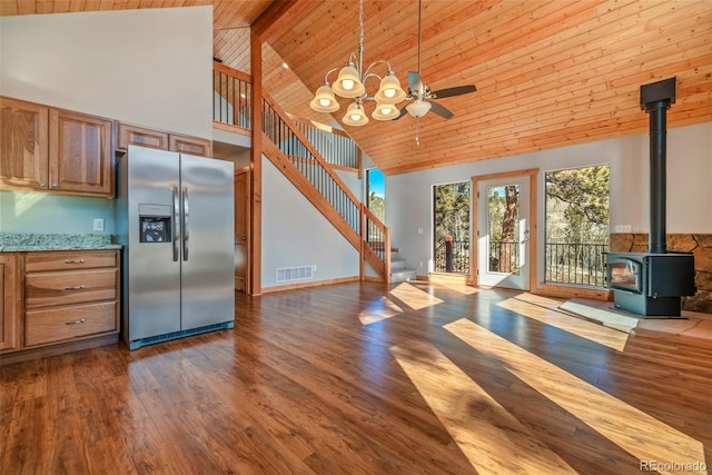 kitchen with stainless steel refrigerator with ice dispenser, wood-type flooring, a wood stove, and light stone counters