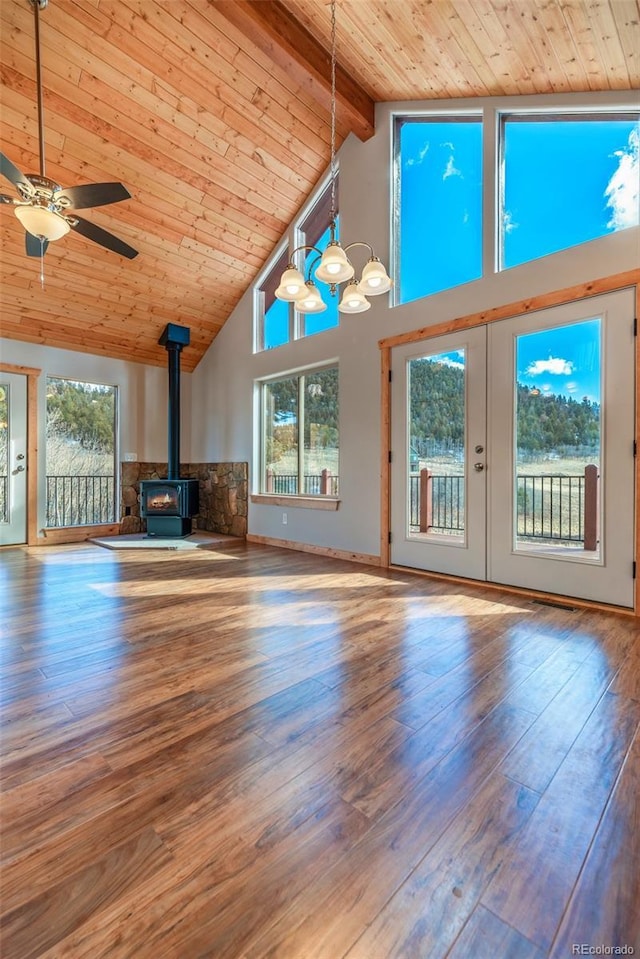 unfurnished living room with beamed ceiling, wood ceiling, a wood stove, hardwood / wood-style flooring, and a healthy amount of sunlight