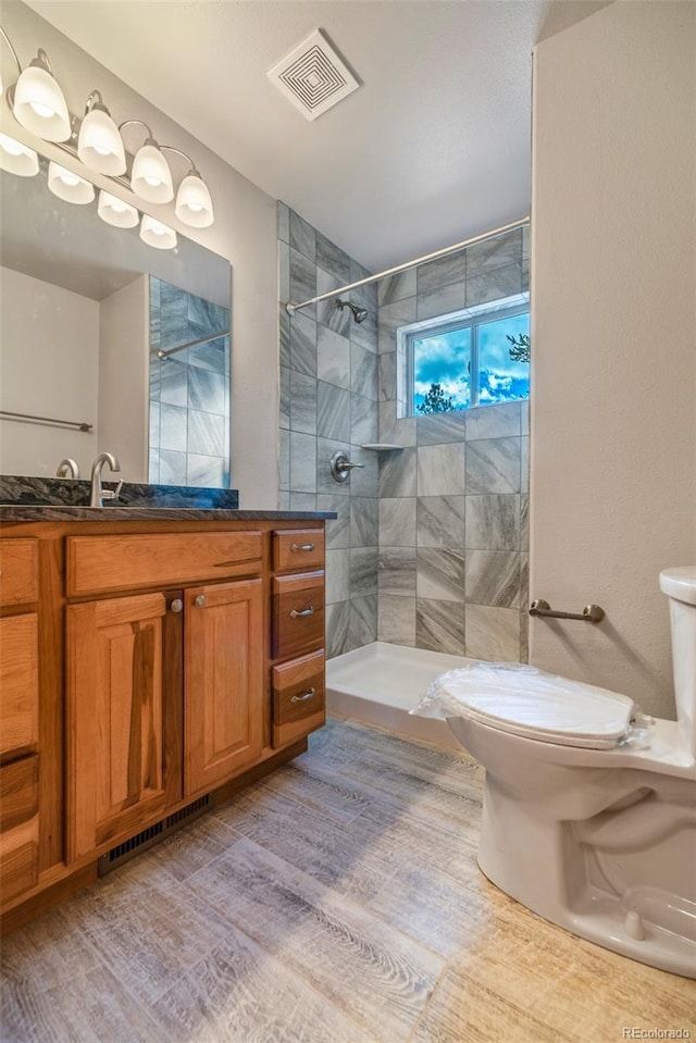 bathroom featuring vanity, wood-type flooring, toilet, and tiled shower