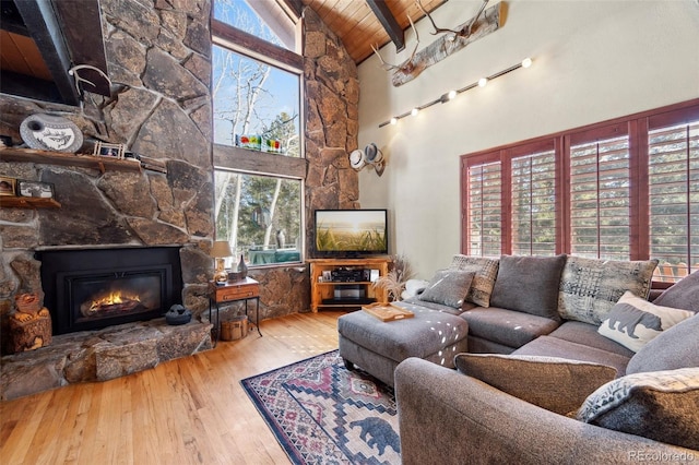 living room featuring wooden ceiling, beamed ceiling, wood finished floors, a stone fireplace, and high vaulted ceiling