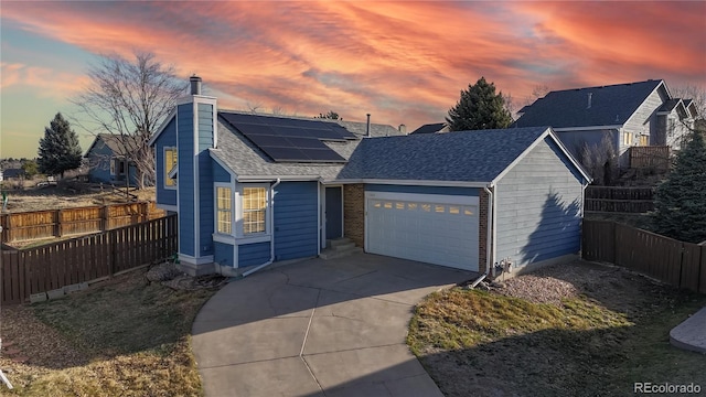 ranch-style house featuring driveway, an attached garage, solar panels, fence private yard, and a chimney