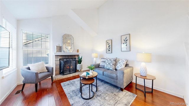 living room featuring visible vents, a brick fireplace, baseboards, and wood finished floors