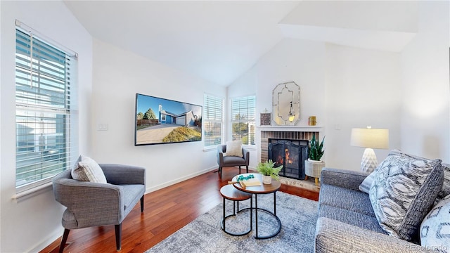 living area with vaulted ceiling, a brick fireplace, wood finished floors, and baseboards