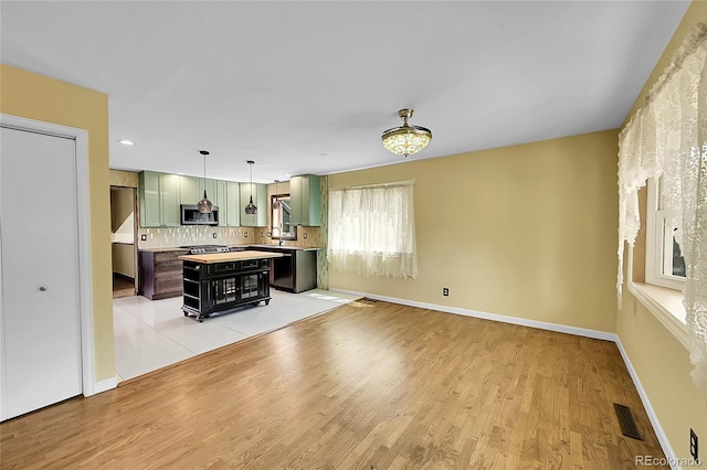 3145 S Bryant St, Sheridan, CO 80110 - kitchen with green cabinets, stainless steel microwave, light countertops, a center island, and light wood finished floors