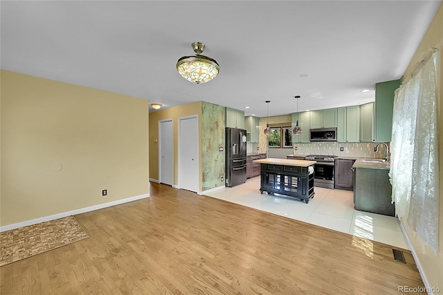 3145 S Bryant St, Sheridan, CO 80110 - kitchen featuring appliances with stainless steel finishes, green cabinetry, a center island, light countertops, and light wood-style floors