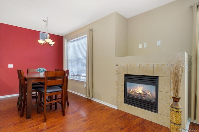 dining room featuring an inviting chandelier, a healthy amount of sunlight, a fireplace, and hardwood / wood-style floors