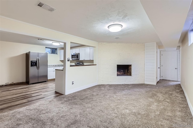 unfurnished living room with visible vents, a textured ceiling, carpet floors, baseboards, and a brick fireplace